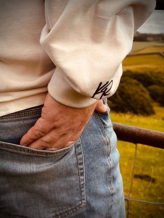 Person wearing a beige Kentucky Ridge sweatshirt with a sleeve logo, standing in a field.