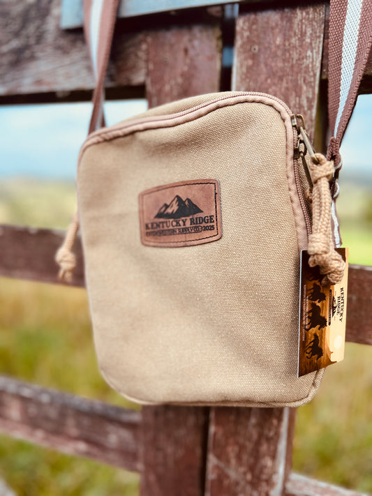 Beige canvas crossbody with a Kentucky Ridge logo attached to a wooden fence.