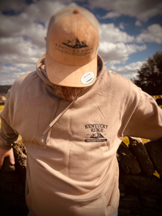 Person wearing a beige hoodie and cap with 'Kentucky Ridge' branding against a cloudy sky.