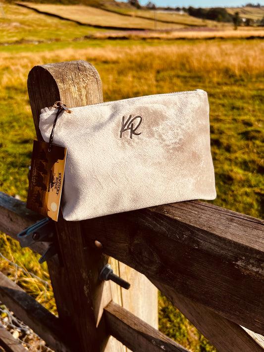 Beige pouch with a logo attached to a wooden fence with a field in the background