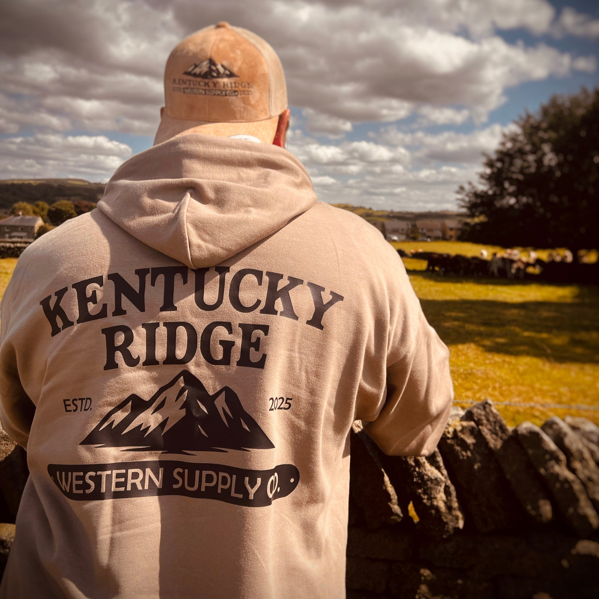 Person wearing a 'Kentucky Ridge Western Supply Co.' hoodie and cap, standing outdoors with a scenic background.