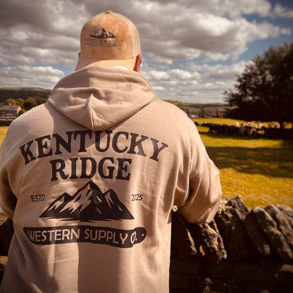 Person wearing a 'Kentucky Ridge Western Supply Co.' hoodie and cap, standing outdoors with a scenic background.