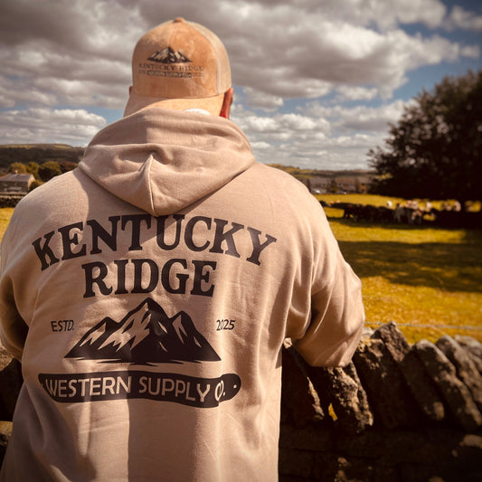 Person wearing a 'Kentucky Ridge Western Supply Co.' hoodie and cap, standing outdoors with a scenic background.