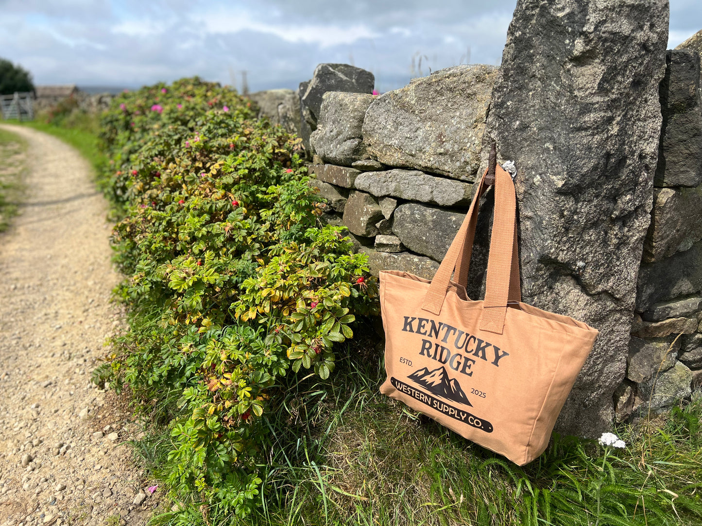 Beige tote bag with 'Kentucky Ridge' branding against a stone wall and natural background