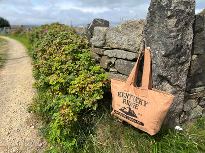 Beige tote bag with 'Kentucky Ridge' branding against a stone wall and natural background