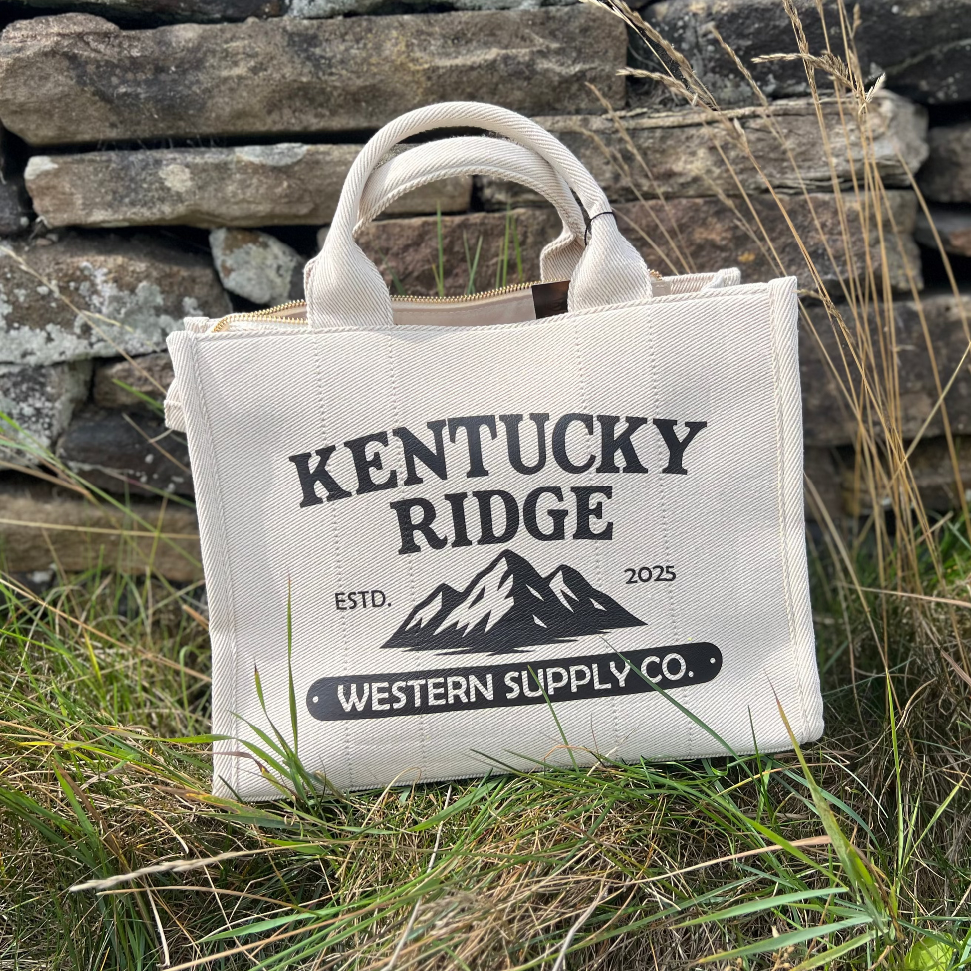 Beige bag with 'Kentucky Ridge' branding against a stone wall and grass background