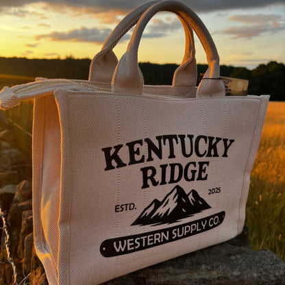 Beige handbag with 'Kentucky Ridge' branding in a field at sunset
