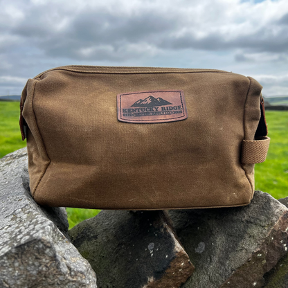 Brown washbag with Kentucky Ridge logo on a stone wall against a green field and cloudy sky