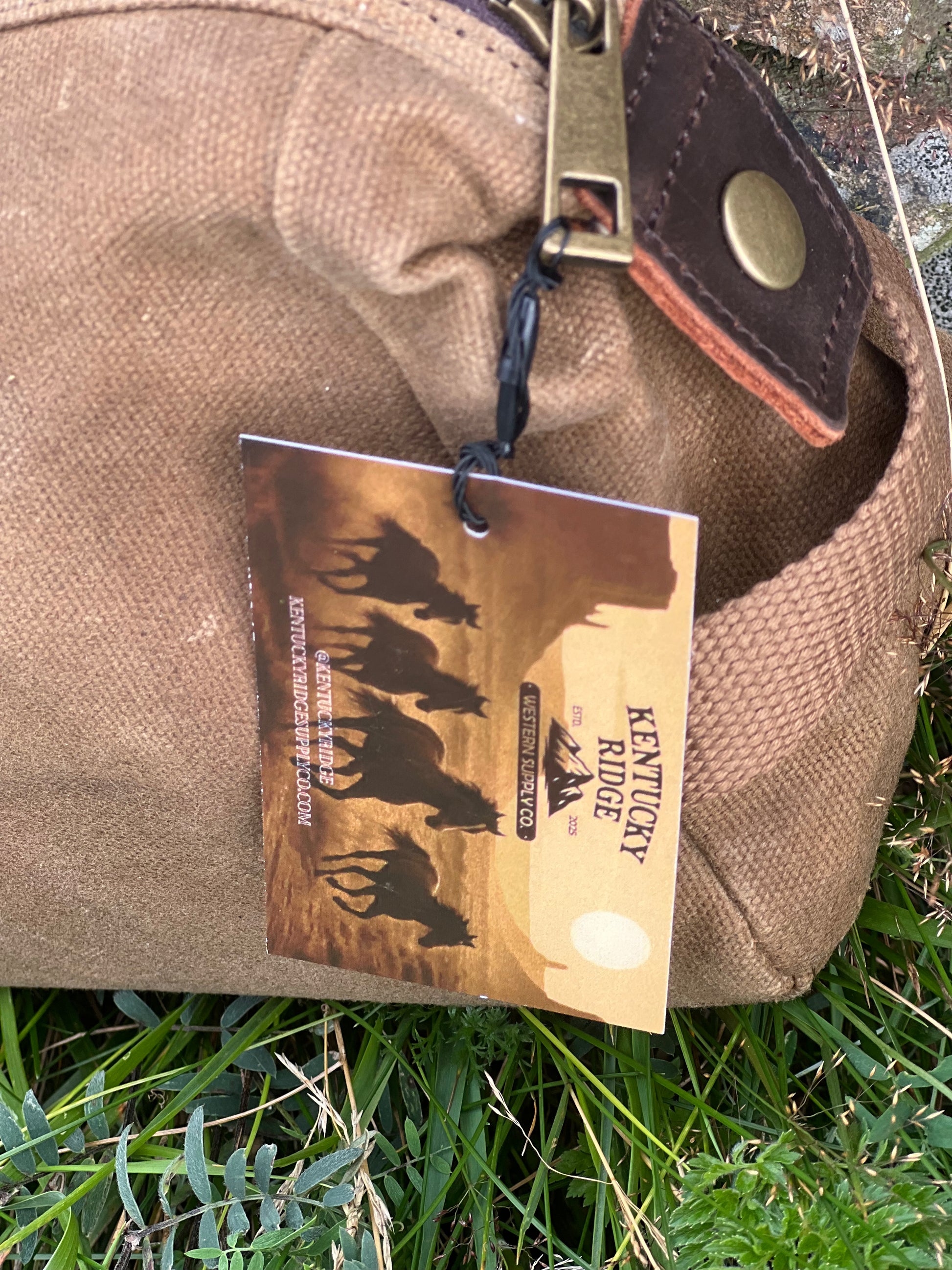 Brown canvas and leather washbag with a tag featuring horse illustrations on grass